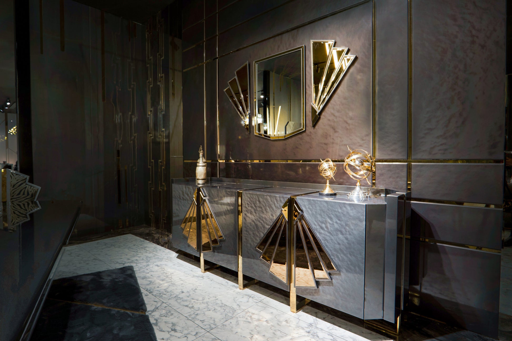 Frost luxury furniture collection featuring geometric wall mirror, dark lacquer sideboard with gold accents, and patterned armchairs with sculptural brass frames.