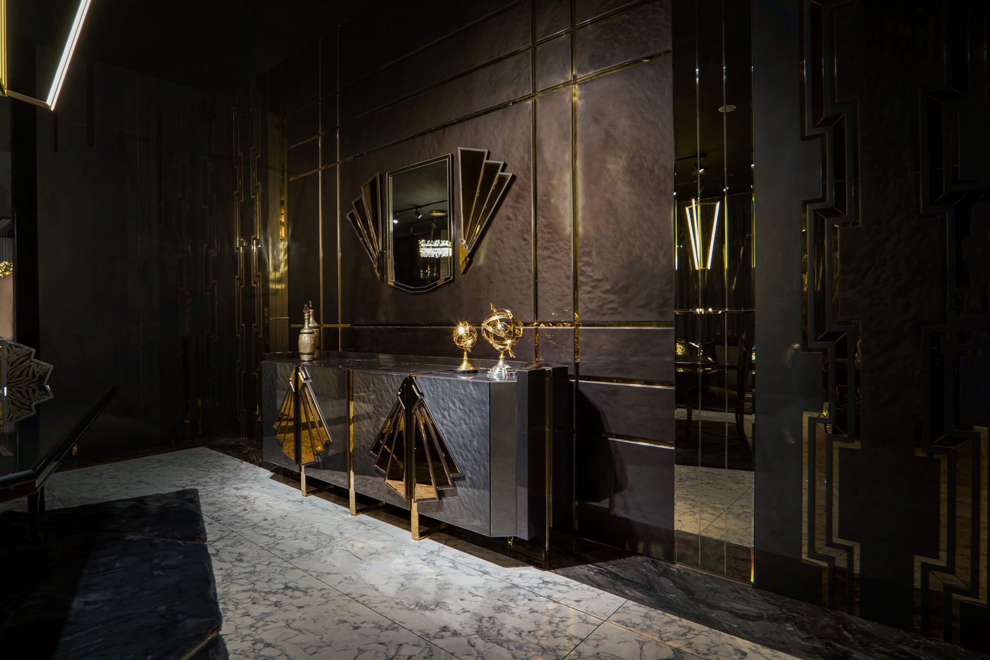 Frost luxury furniture collection featuring geometric wall mirror, dark lacquer sideboard with gold accents, and patterned armchairs with sculptural brass frames.