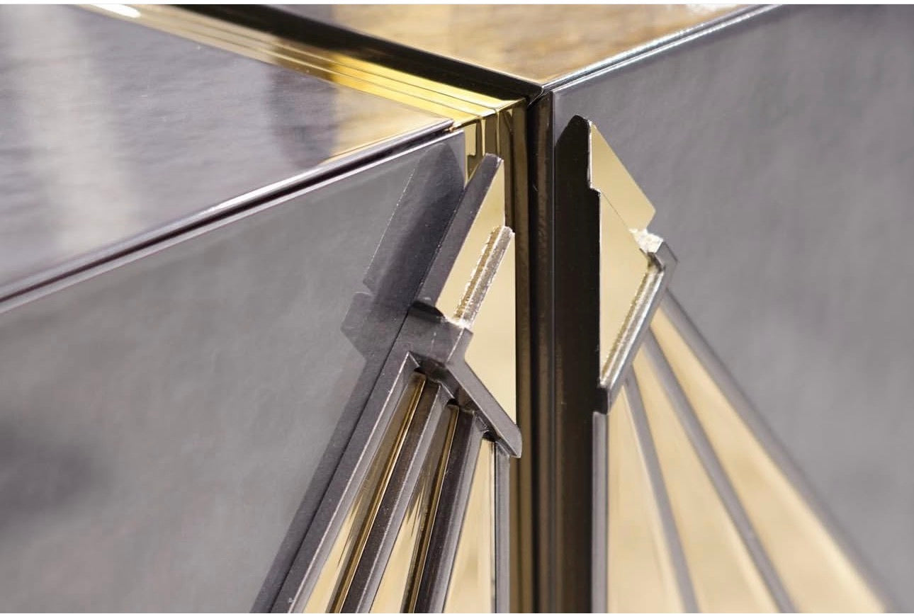 Frost luxury furniture collection featuring geometric wall mirror, dark lacquer sideboard with gold accents, and patterned armchairs with sculptural brass frames.