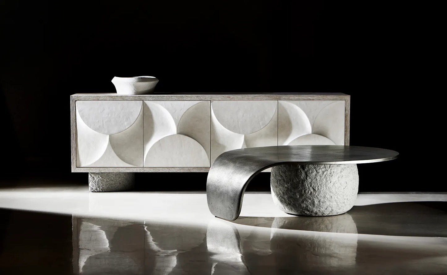 Fancci Velune sculptural cocktail table with curved metal top and stone base in a modern luxury living space.